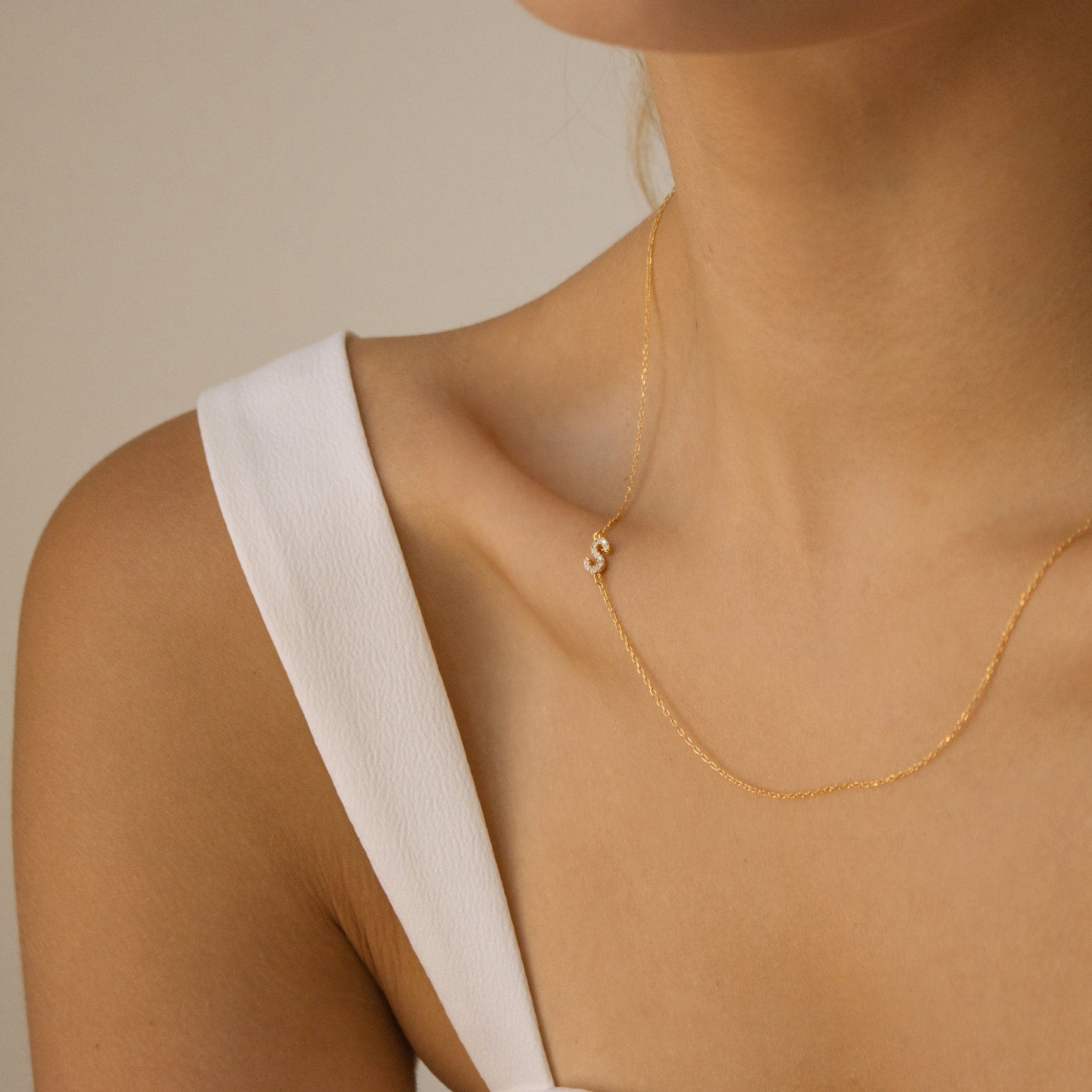 A woman wearing a Pave Sideways Initial Necklace with an S pendant and a white sleeveless top.
