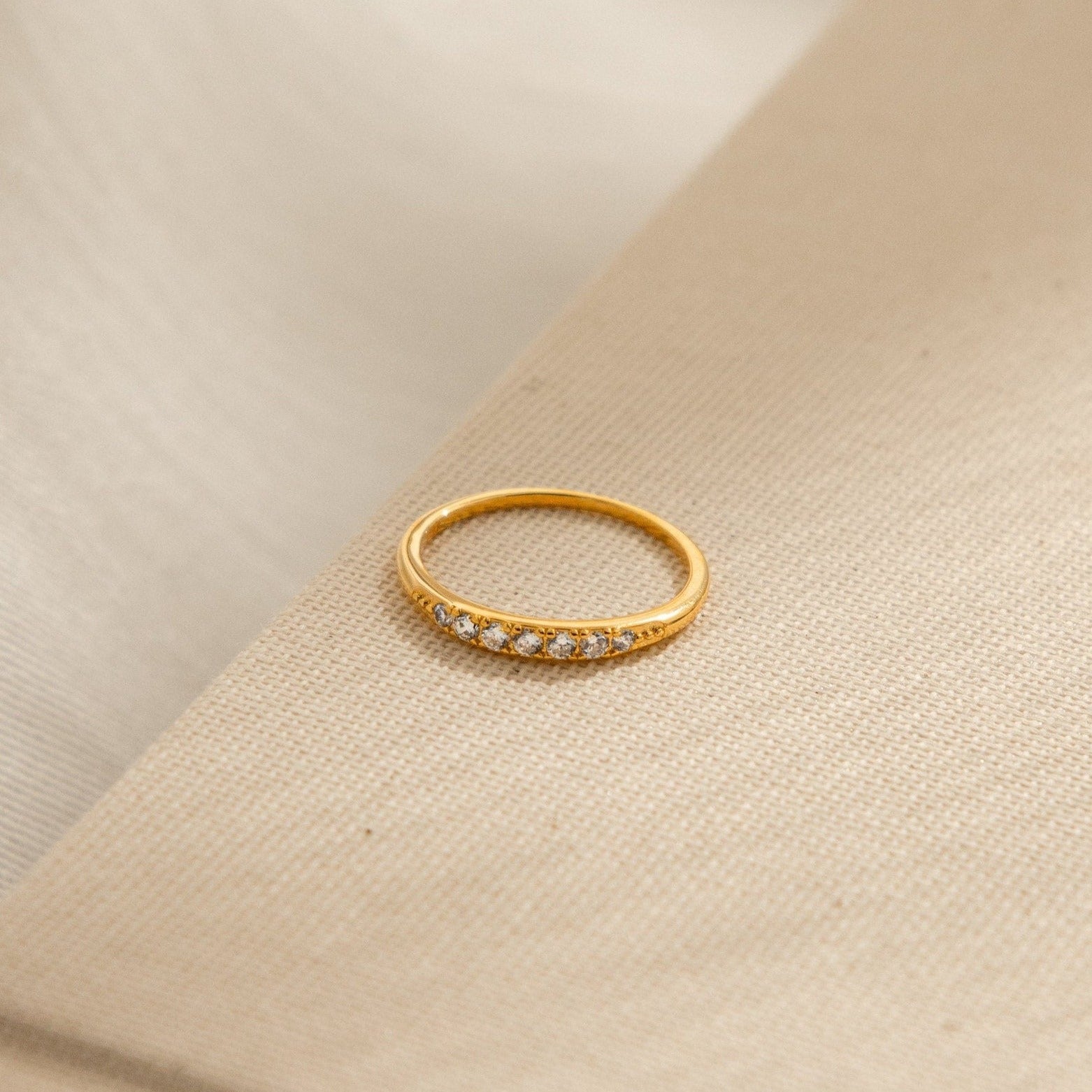 The Lace Pave Ring, a delicate diamond band, is displayed on a beige textured fabric.
