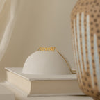 Nella Name Necklace in Box Chain displayed on a white dome, next to a book and patterned vase.