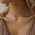 Close-up of a woman wearing the Paris Multiple Name Necklace in gold with Bailey and Amelia pendants, styled with taupe fabric.