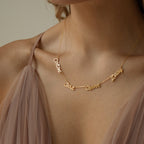 A woman wearing the Paris Multiple Name Necklace, inspired by Parisian style, paired with a sheer mauve spaghetti strap dress.