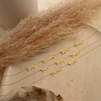The Mellow Multiple Name Necklace is displayed on a light wooden surface with dried pampas grass, making this elegant personalized jewelry a thoughtful gift for mom.