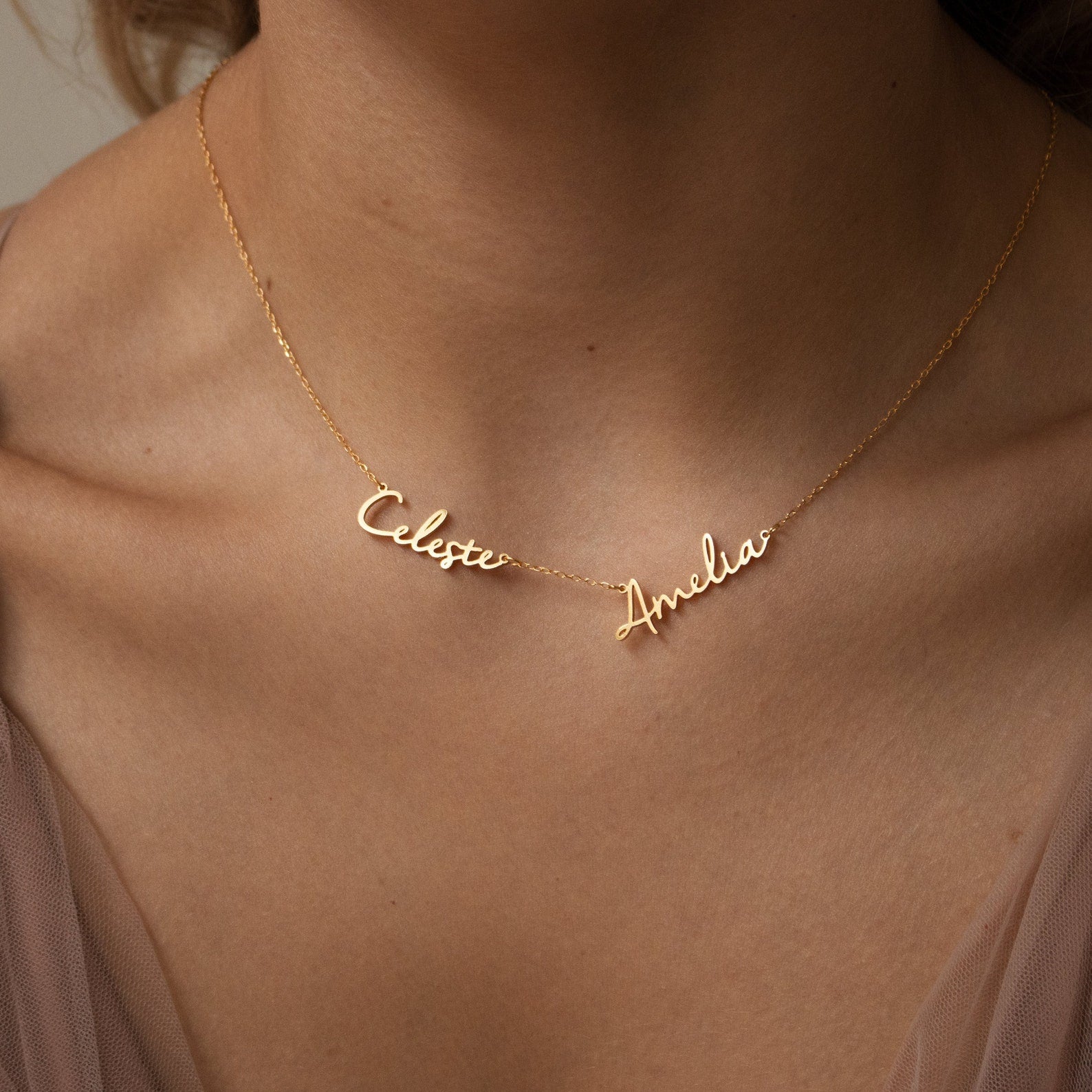 The Nella Multiple Name Necklace displays the names Celeste and Amelia in elegant cursive, beautifully worn around a woman's neck.