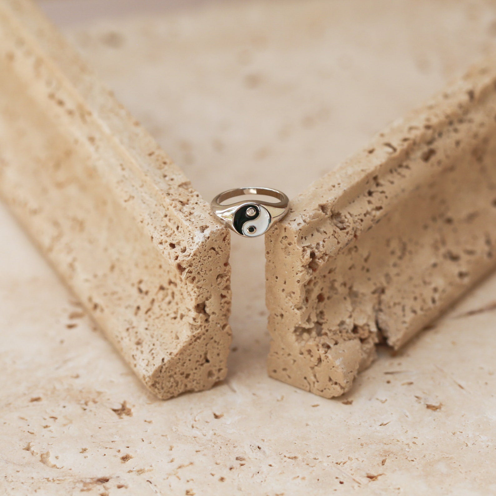 The Yin Yang Ring, featuring a silver enamel-finished signet, rests gracefully between two pieces of textured beige stone.