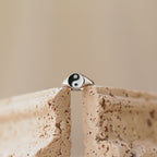 A Yin Yang Ring with a silver enamel finish balances on the edge of a textured beige stone, set against a softly blurred background.