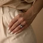 A hand with pale nail polish wears the Yin Yang Ring with an enamel finish, resting on cream-colored pants.