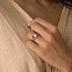 A hand wearing the Yin Yang Ring gently holds the collar of a beige textured shirt.