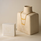 London Double Name Necklace in Box Chain with a chic font on a beige display, next to a white Caitlyn Minimalist jewelry box—perfect personalized jewelry for any occasion.