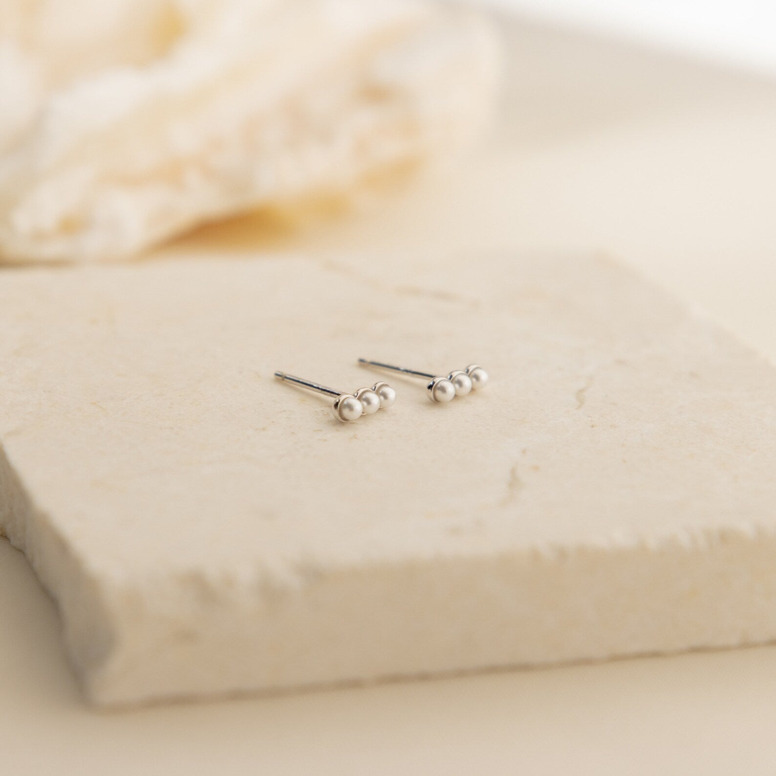 Tiny Pearl Bar Studs displayed on a textured beige stone surface—delicate freshwater pearl earrings that are perfect for elegant everyday wear.