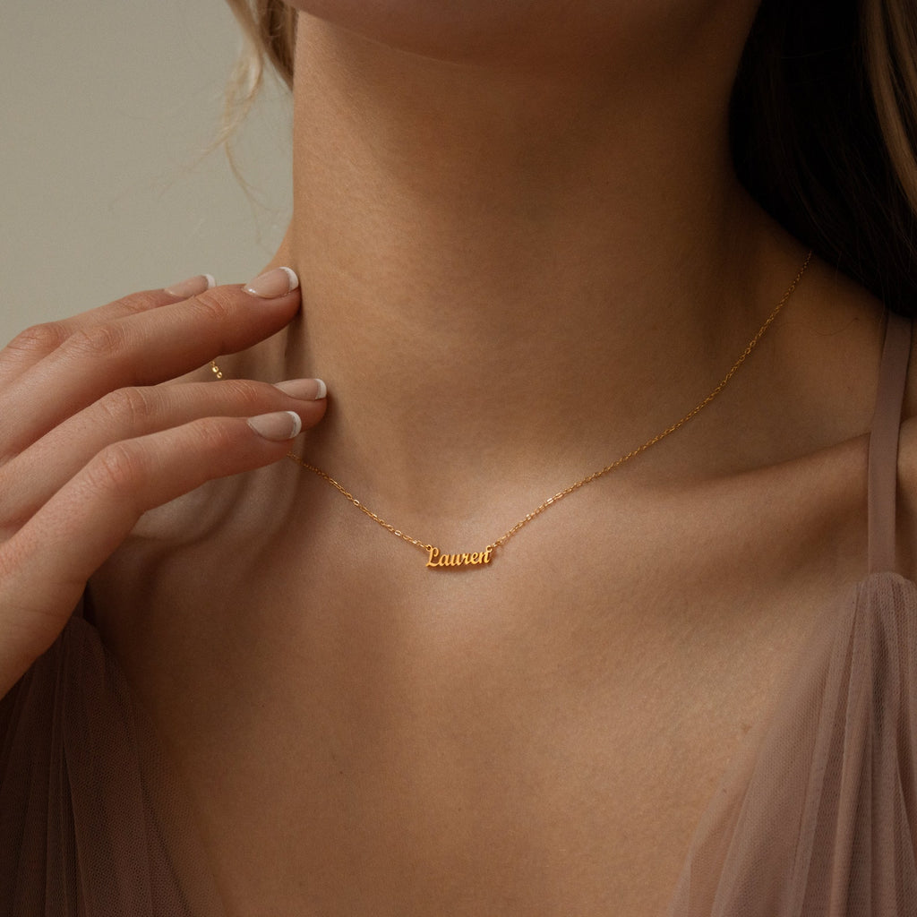 Close-up of a woman wearing the Tiny London Name Necklace, a customizable gold name plate with "Lauren" in elegant cursive lettering.