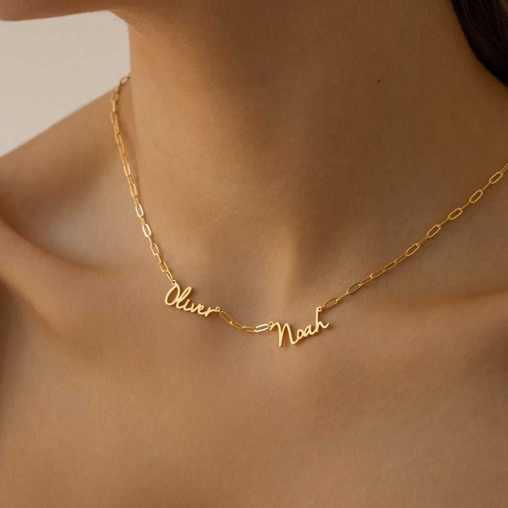 Close-up of the Nella Multiple Name Necklace in Paperclip Chain, showcasing “Oliver” and “Noah” in cursive script on a woman’s neck with a bold paperclip chain for added elegance.