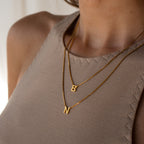 Close-up of a woman wearing the Alice Double Letter Necklace in Box Chain with B and N gold letter pendants over a beige top.