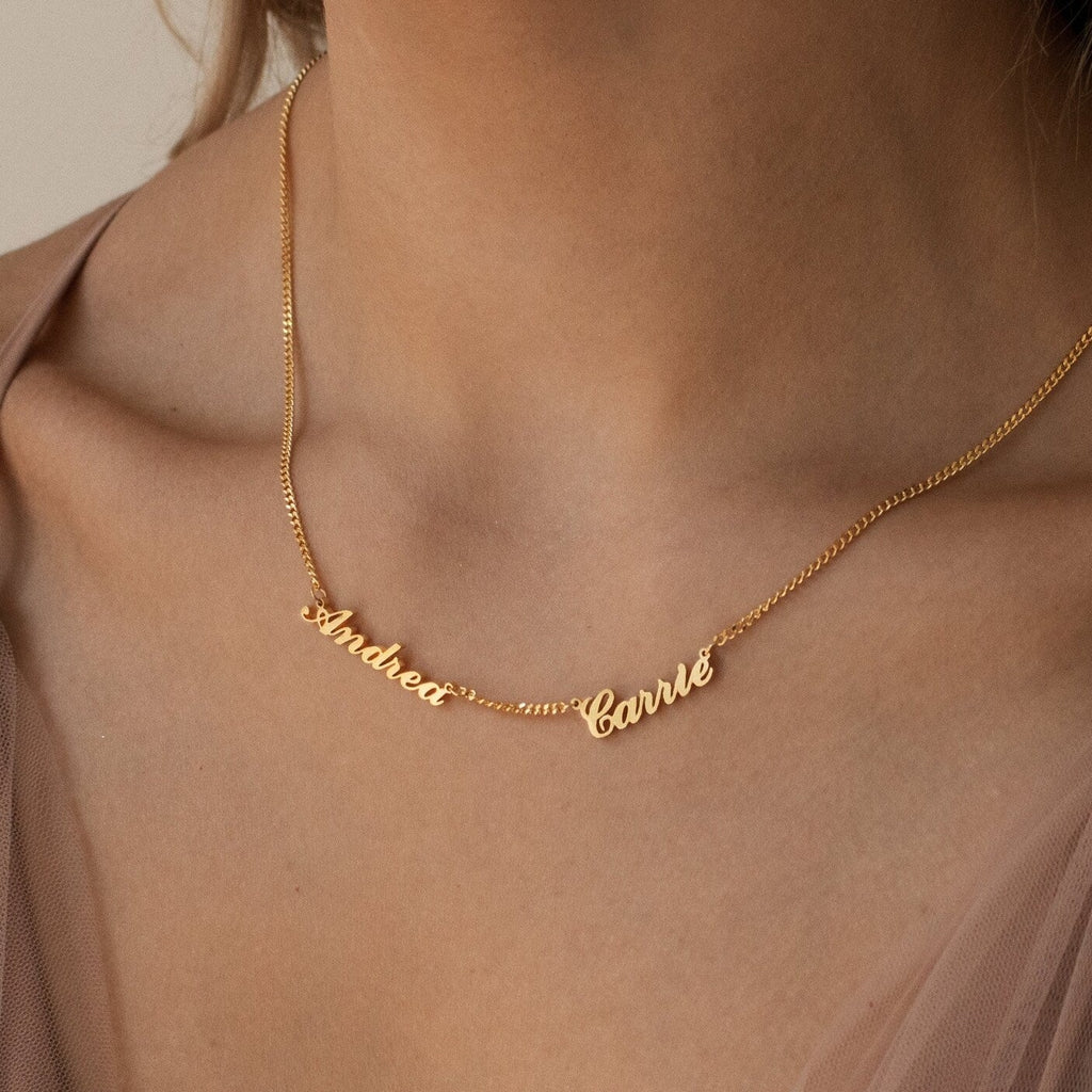 A woman wears a personalized jewelry piece—a Carrie Multiple Name Necklace in Curb Chain with the names Andrea and Carrie in elegant cursive letters.