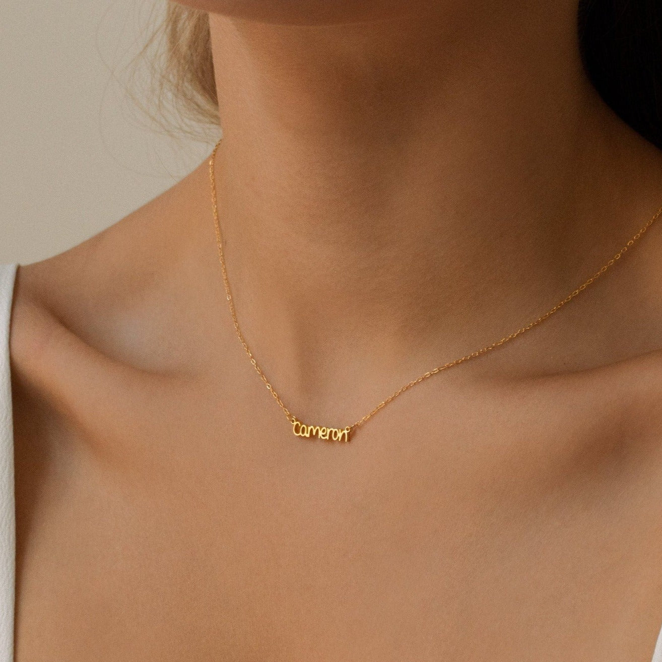 A woman wears a gold Tiny Preppy Name Necklace with "cameron" in a playful, youth-inspired font.