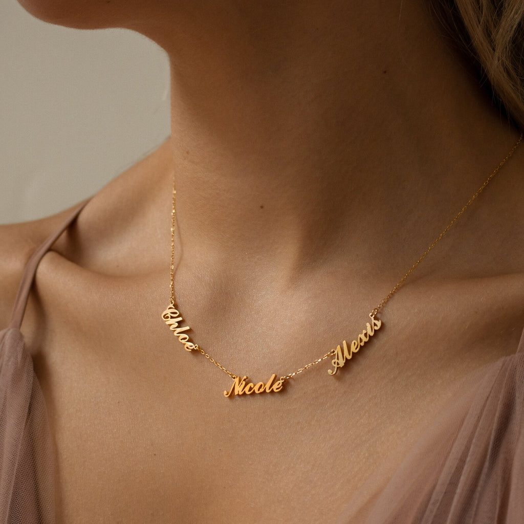 The Carrie Multiple Name Necklace in Rose Gold features personalized names on a dainty chain, elegantly displayed above a sheer top—a stunning example of custom jewelry.
