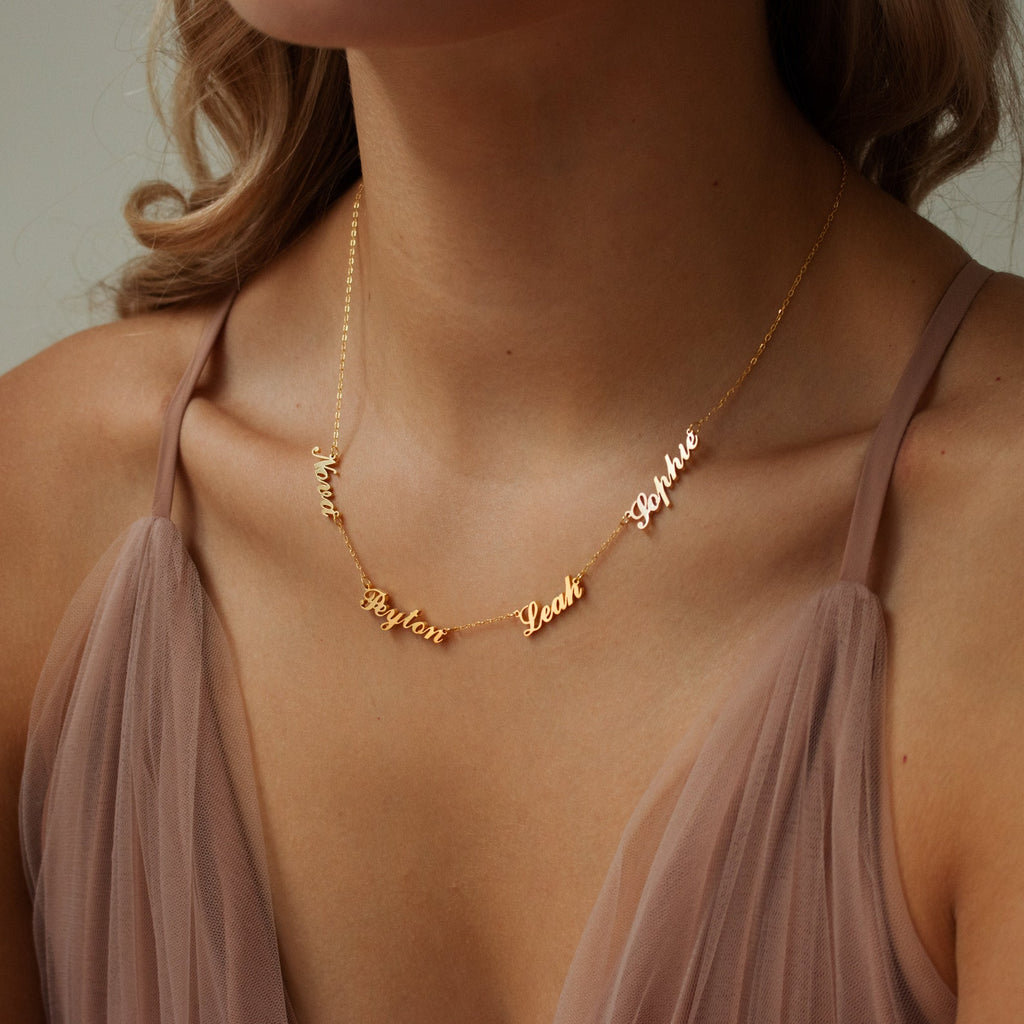 A woman wearing the Carrie Multiple Name Necklace in gold, personalized with the names Noah, Peyton, Leah, and Sophie.