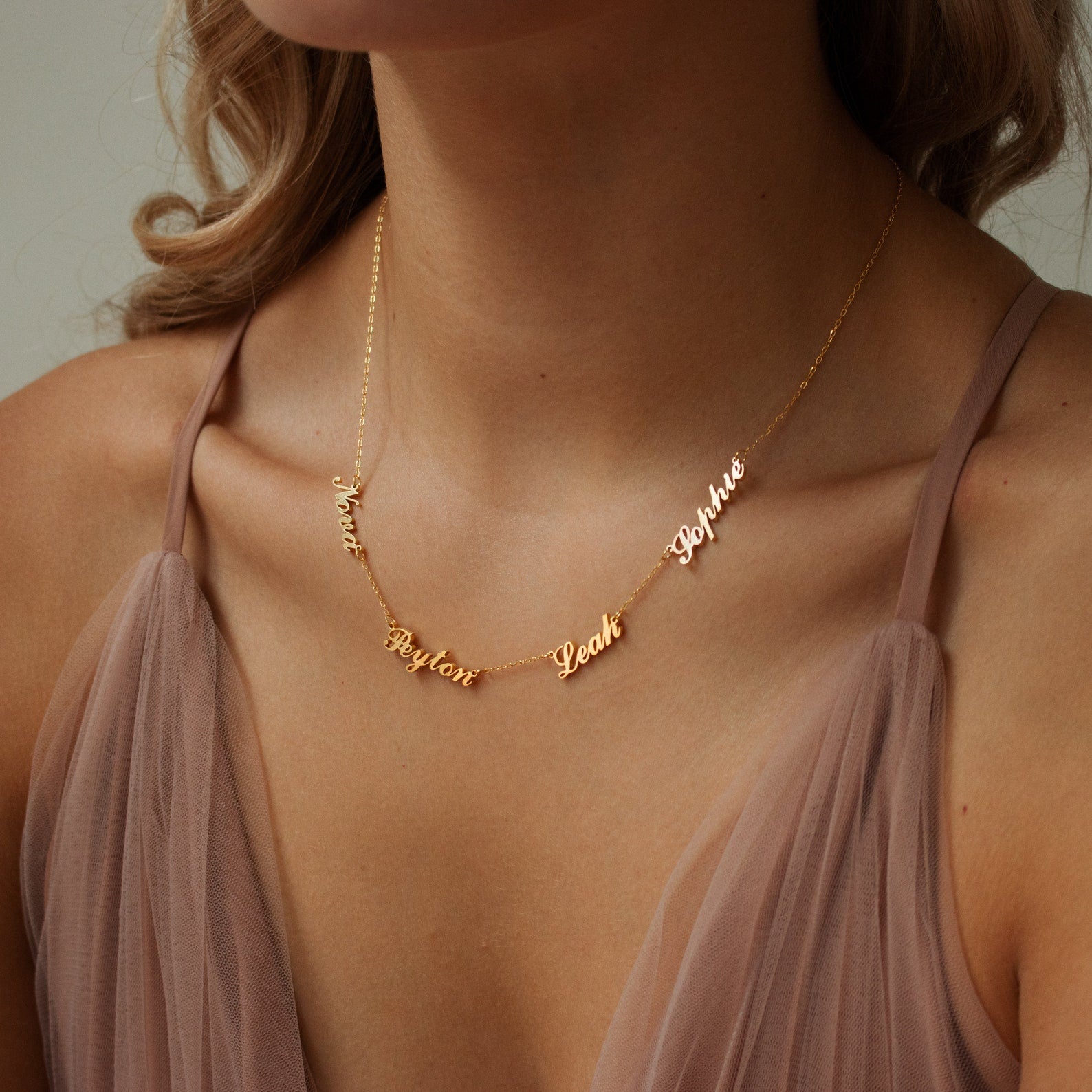 A woman wearing the Carrie Multiple Name Necklace in gold, personalized with the names Noah, Peyton, Leah, and Sophie.