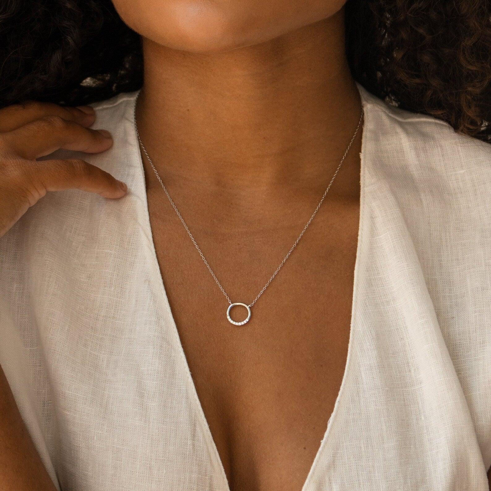 A woman wears a white blouse and the Kayla Pave Circle Necklace, highlighting her preference for minimalistic jewelry.