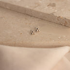 Trio Sphere Studs in silver are displayed on a beige stone surface with soft fabric in front—ideal for stacking or unique piercings.