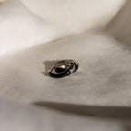 Black Enamel Huggies rest on a soft, light-colored fabric, highlighted by gentle shadows.