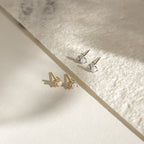 A pair of Jackie Opal Studs in gold and another in silver, each featuring small round gemstones, rest elegantly on a textured surface.