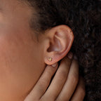A close-up of a person’s ear showcases the Trio Sphere Studs—small gold earrings styled as part of an elegant earring stack.