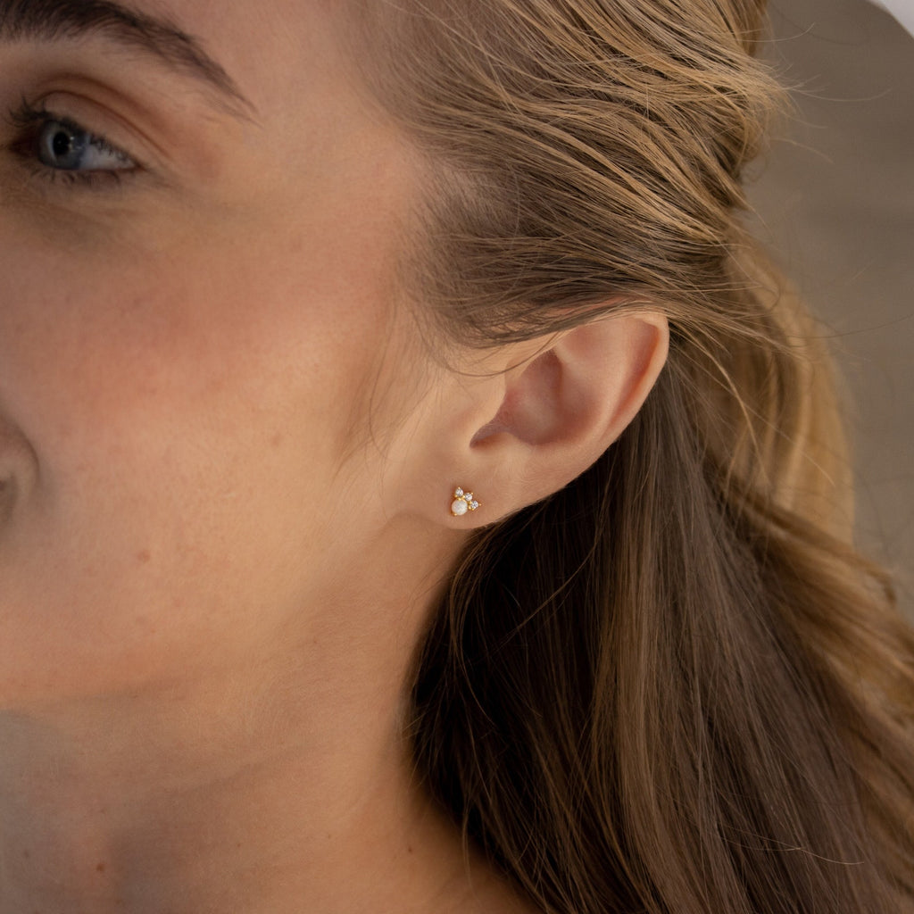 Close-up of a woman's ear wearing the Dainty Opal Earrings Set with gold and pearl accents, her brown hair tucked behind her ear for a delicate look.