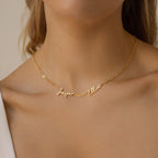 A woman wears the Nella Multiple Name Necklace in a bold paperclip chain, showcasing the names Jasper and Elliot in elegant cursive script.