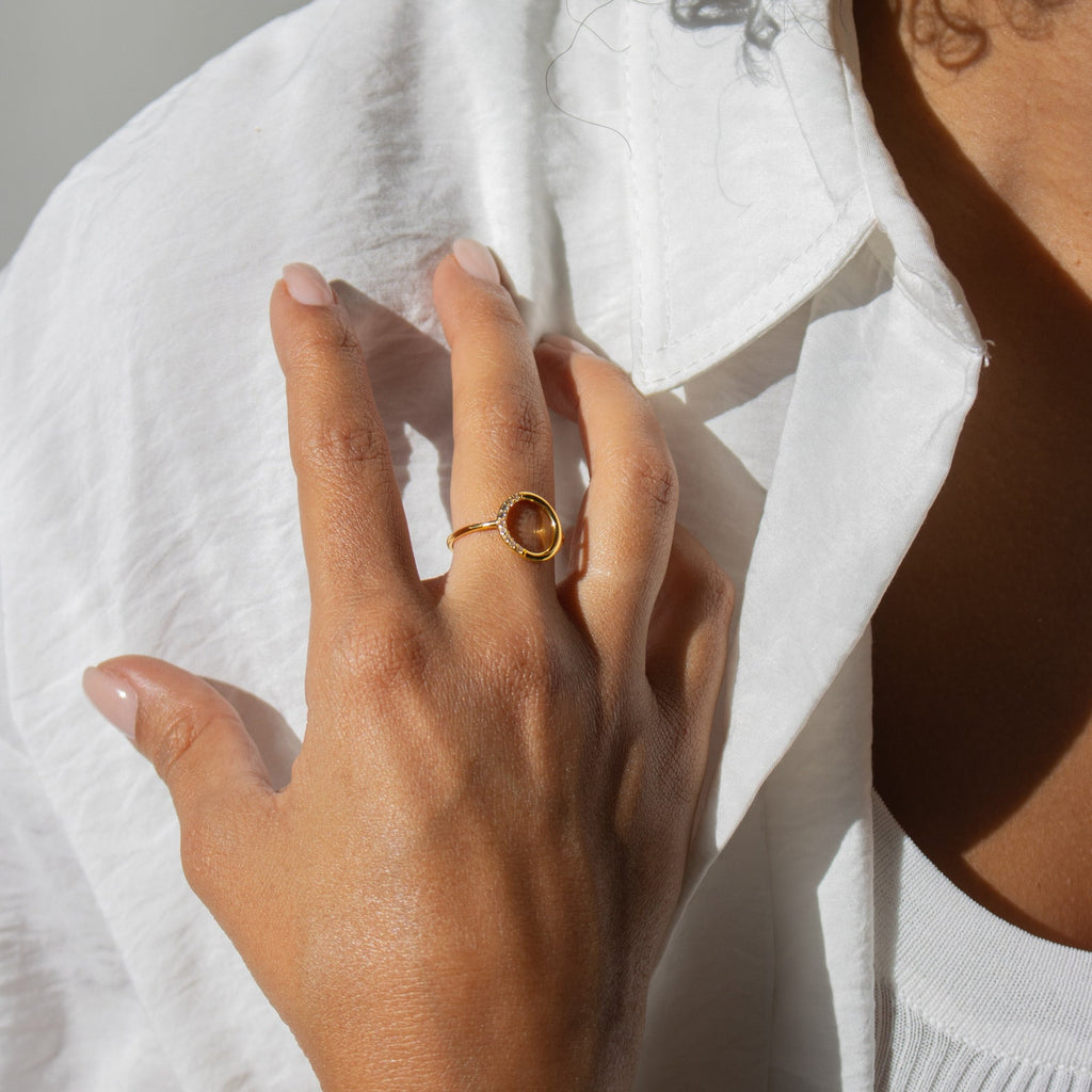 A hand wearing the Pave Open Circle Ring rests on a chest in natural light, styled with a white shirt and white ribbed top.