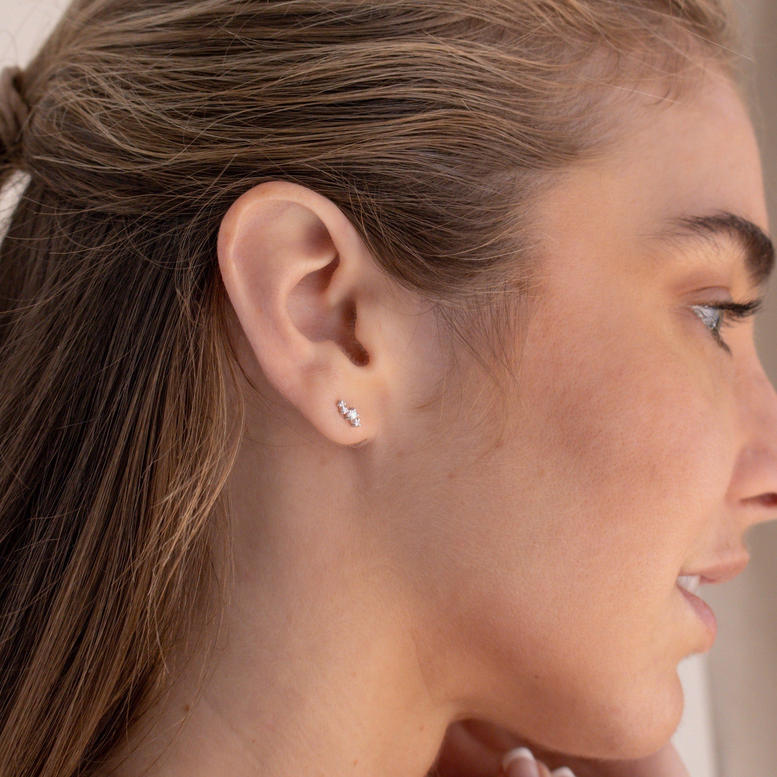 Close-up of a woman's ear wearing the Nile Opal and Diamond Studs, delicate silver earrings featuring three clustered stones for a constellation-inspired look.