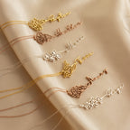 Six Flower Name Necklaces are displayed on beige fabric; each features a unique name and a vibrant birth flower design.