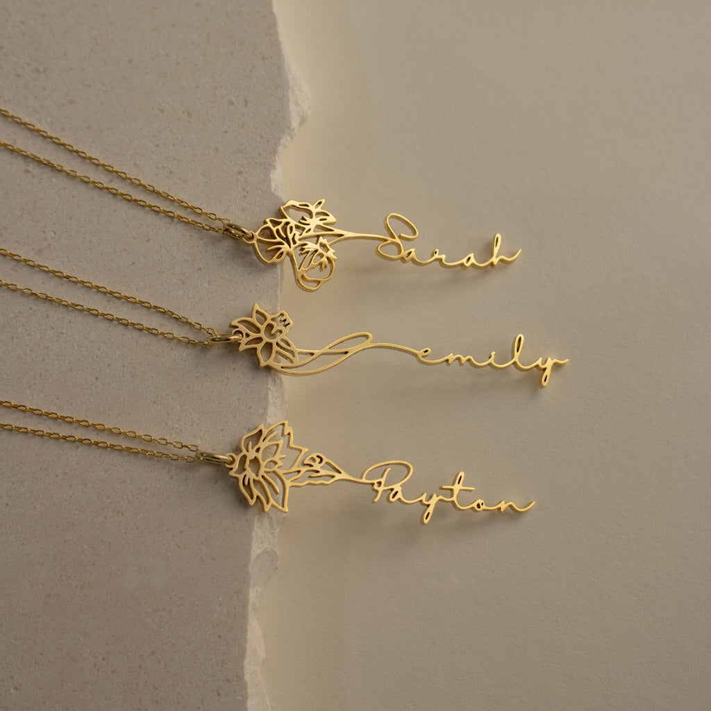 Three gold Flower Name Necklaces, each with a unique floral design and personalized with the names Sarah, Emily, and Payton plus their birth flowers, are displayed on a neutral background.