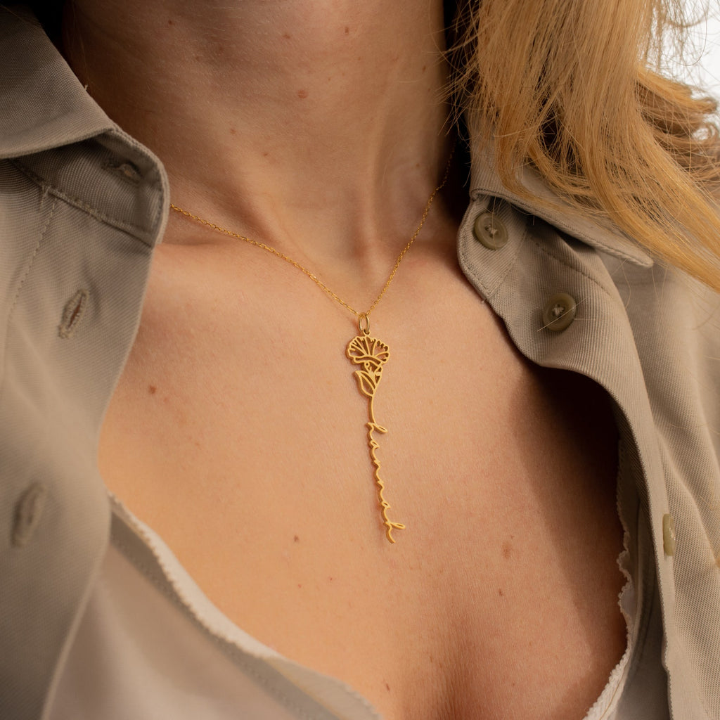 A woman wears a gold Flower Name Necklace with a tree and branch design, paired with a beige, partially unbuttoned shirt.