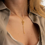 A woman wears a gold Flower Name Necklace with a tree and branch design, paired with a beige, partially unbuttoned shirt.
