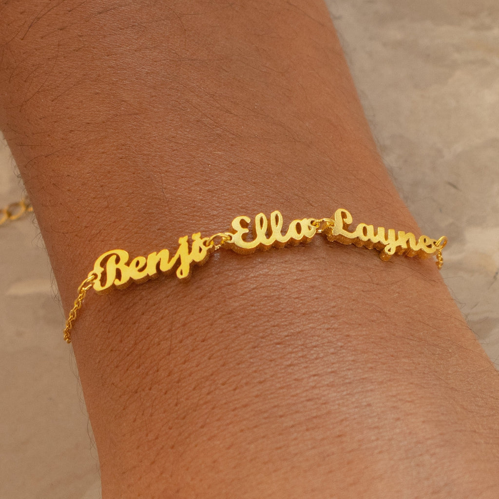 The London Multiple Name Bracelet elegantly displays the names Benji, Ella, and Layne in cursive, creating a dainty personalized accessory for your wrist.