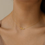 A woman wears the Tiny Grace Name Necklace, a gold necklace featuring a custom nameplate pendant.