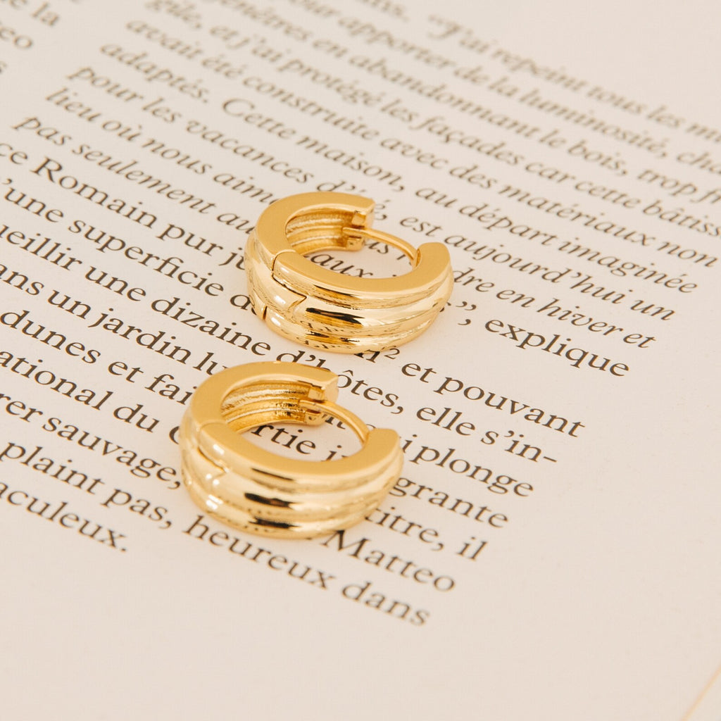 The Canal Chunky Hoops rest on an open book with French text, bringing a modern twist to classic everyday earrings.