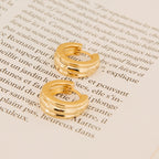 The Canal Chunky Hoops rest on an open book with French text, bringing a modern twist to classic everyday earrings.