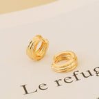 The Canal Chunky Hoops feature a layered gold design, resting on paper with partial text reading "Le refugi"—perfect as contemporary huggies or stylish everyday earrings.