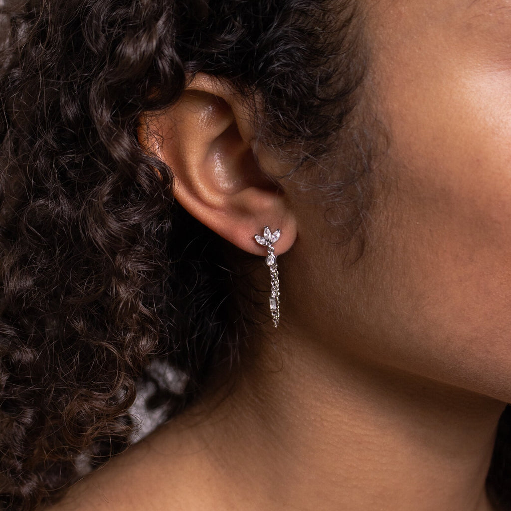 Close-up of a person with curly hair wearing Genesis Chain Earrings—sparkling, silver, leaf-shaped statement jewelry.
