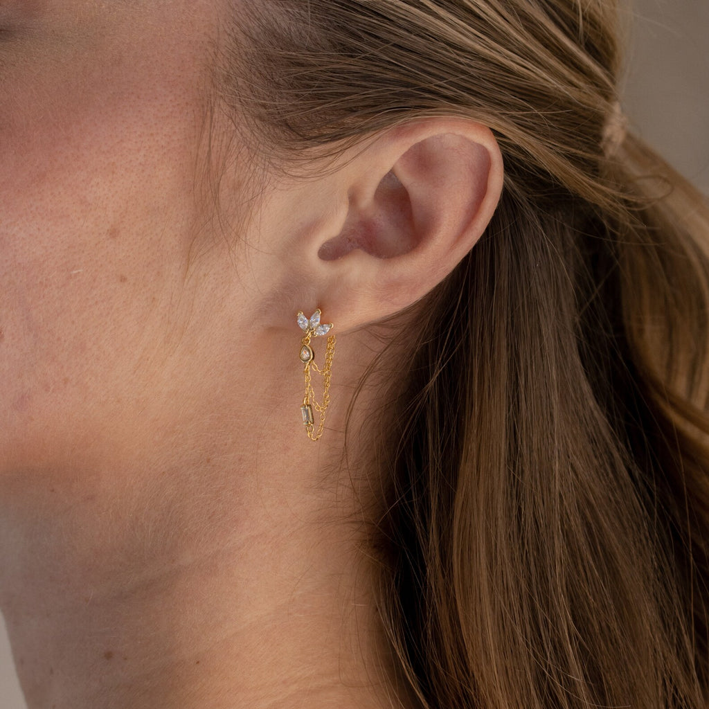 Close-up of a woman's ear wearing Genesis Chain Earrings—gold chains with small crystal accents, ideal for adding statement jewelry flair to any outfit.