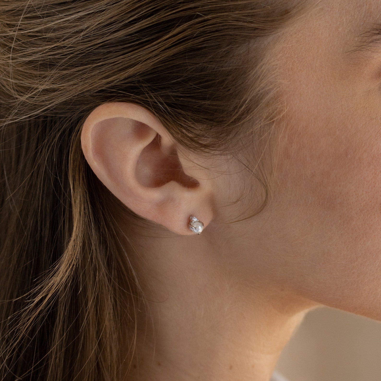Close-up of a woman's ear wearing the Julia Pearl Studs, featuring small, round freshwater pearls.