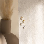Julia Pearl Studs in gold and silver are displayed on a textured surface next to a matte vase with dried pampas grass.