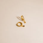 The Emily Pave Star Huggies feature gold hoops with star charms and embedded crystals, creating a celestial sparkle against a light beige background.