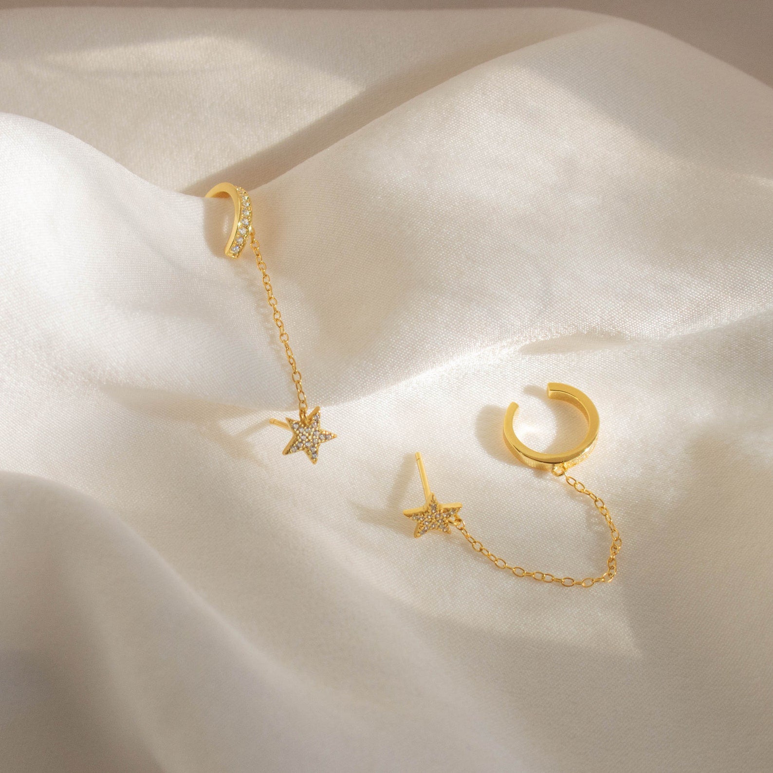 Star Pave Chain Ear Cuffs—gold earrings with diamond-studded star charms and delicate chains—displayed on soft white fabric.