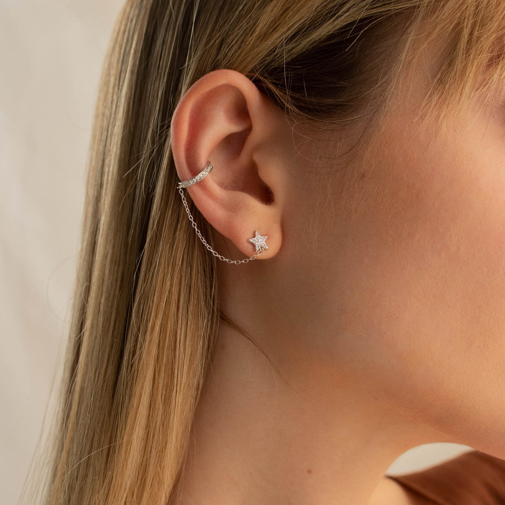 Close-up of a woman's ear wearing Star Pave Chain Ear Cuffs with a diamond-studded star charm and an adjustable chain connecting to the upper ear.