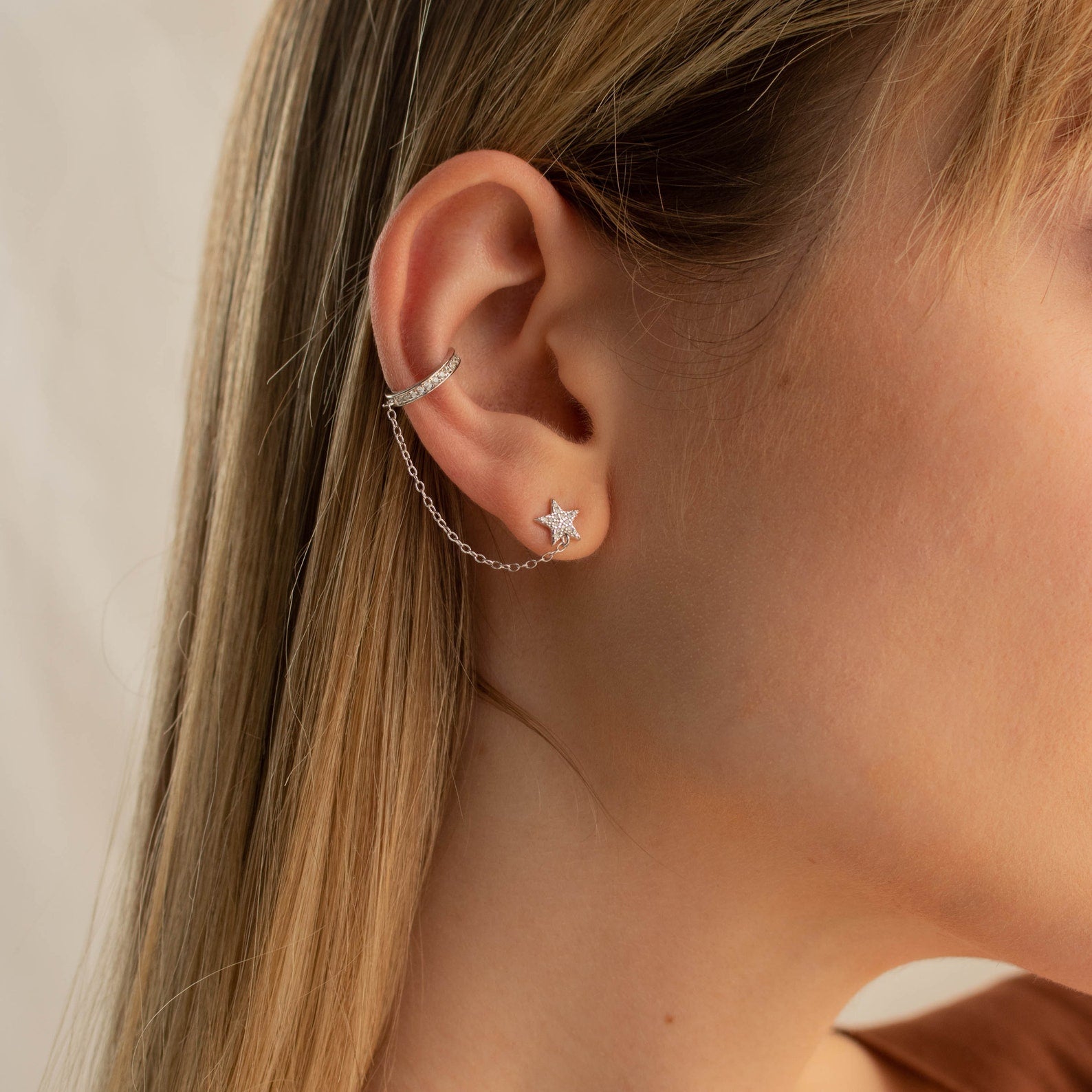 Close-up of a woman's ear wearing Star Pave Chain Ear Cuffs with a diamond-studded star charm and an adjustable chain connecting to the upper ear.