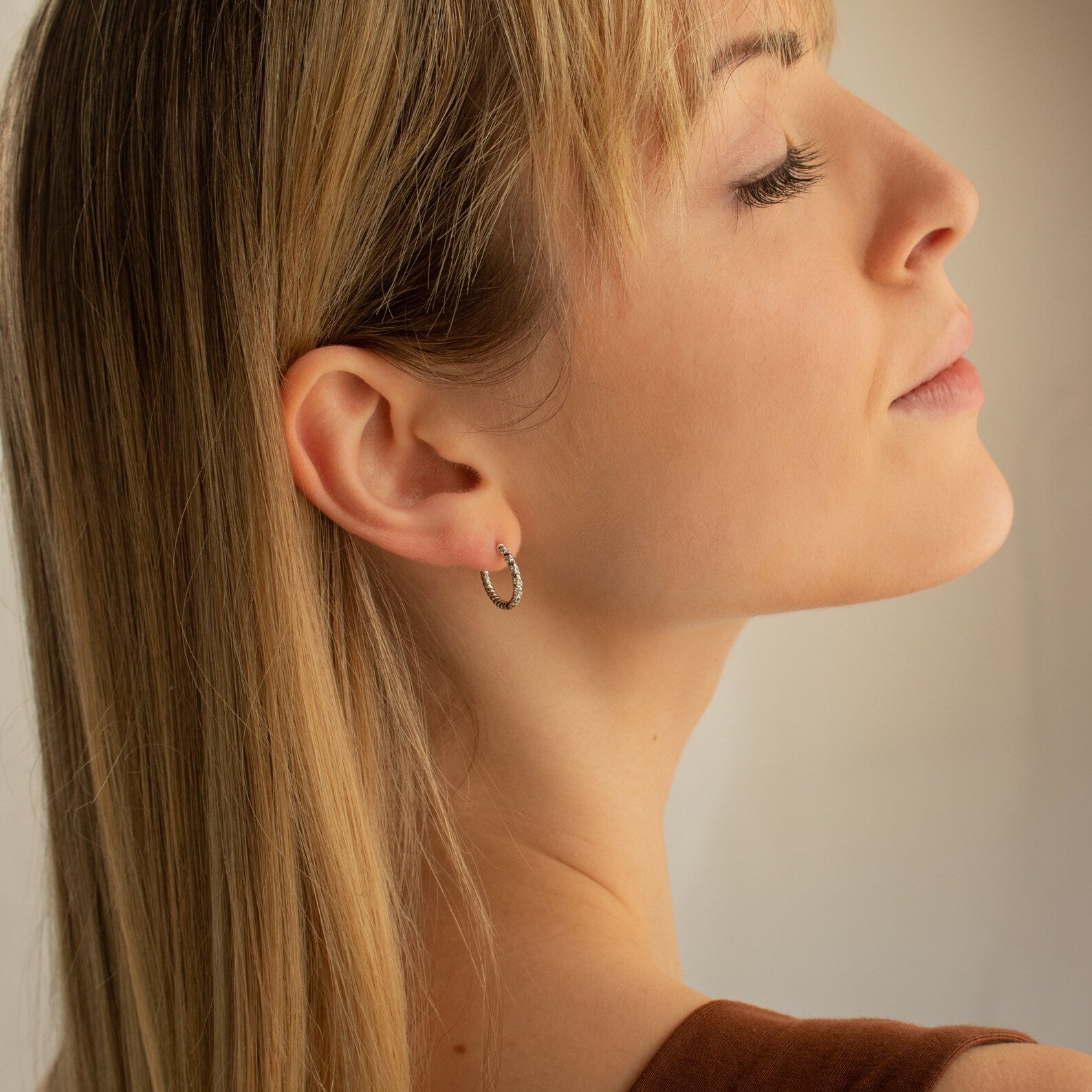 Blonde woman in profile with eyes closed, wearing Aster Pave Twisted Hoops in soft lighting.