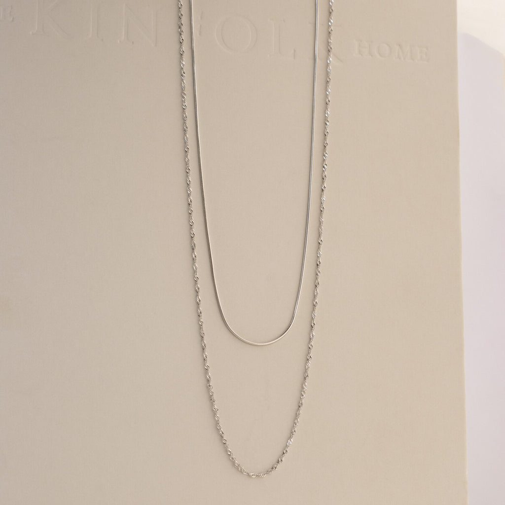 The Monet Duo Chain, with a sleek snake and elegant Singapore chain design, is displayed on a light beige background.