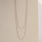 The Monet Duo Chain, with a sleek snake and elegant Singapore chain design, is displayed on a light beige background.